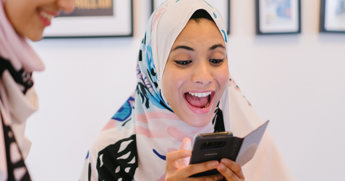 Two people in hijabs smile at cellphone
