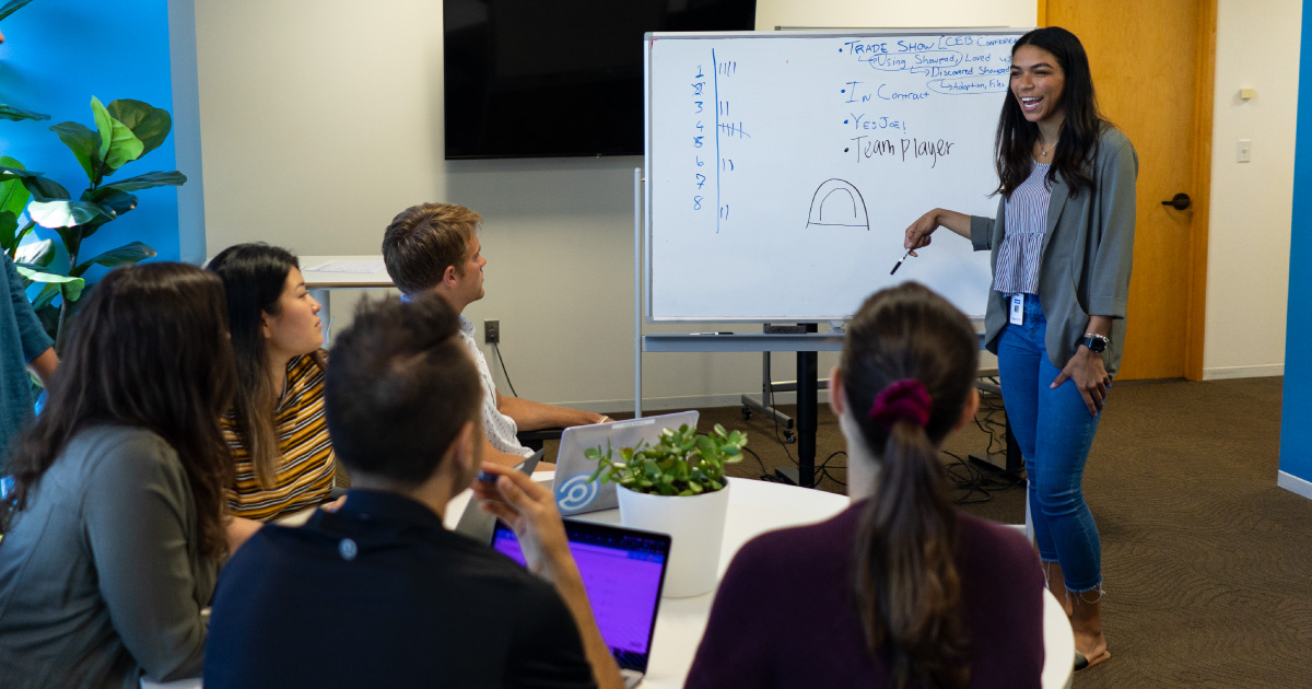 Person in front of whiteboard presents to a seated team