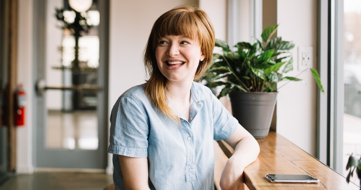 Person smiles in front of wooden table