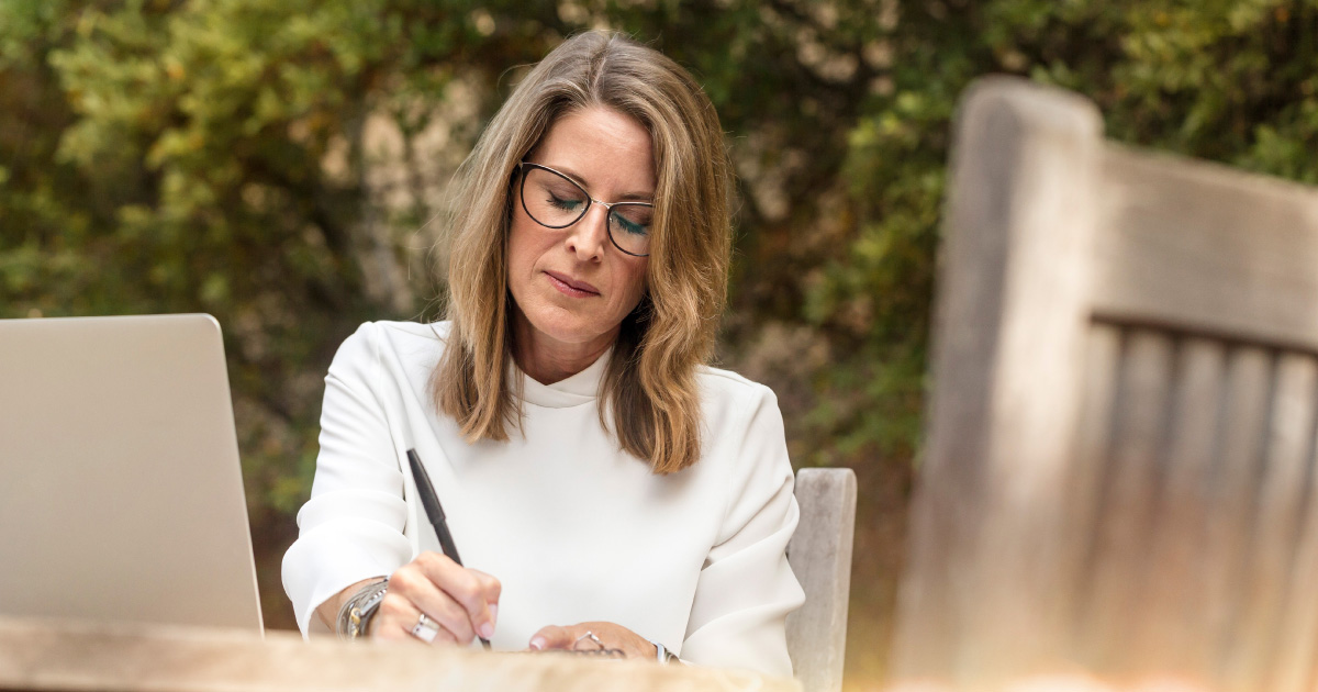 Person in glasses thoughtfully writes a note in front of computer