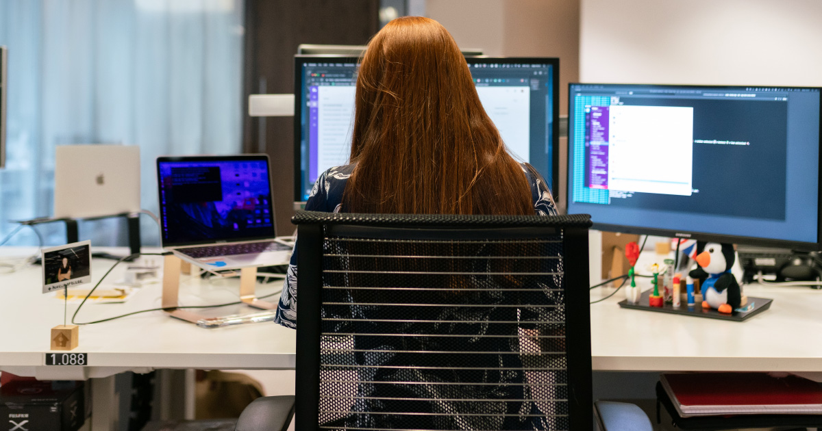 Person sits in front of three computers and a standing phone