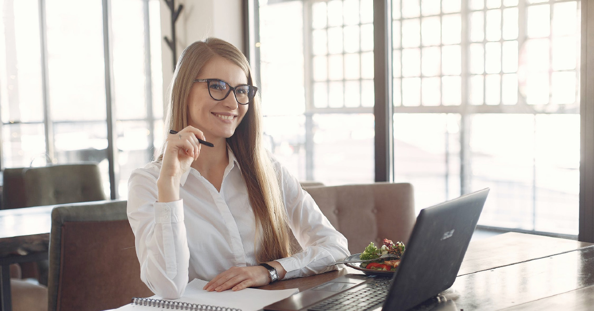 Person smiling into the distance while seated at desk with paper notebook and computer