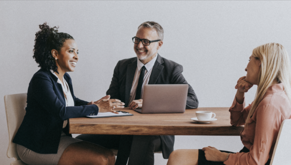 Three people in suits smiling at a desk