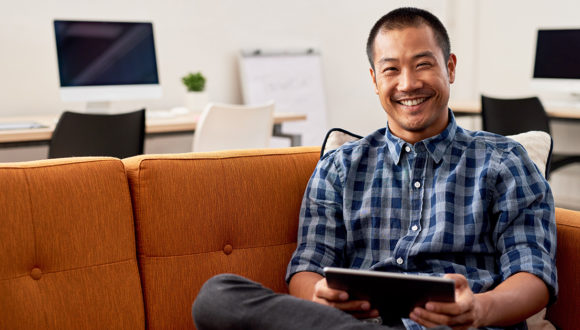 Smiling person holding tablet on couch