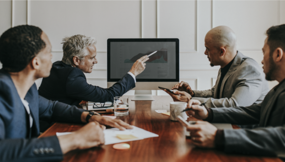 Four people sitting at a desk review a graph on a screen