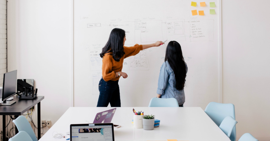 Two people look at sales asset management notes on a large board