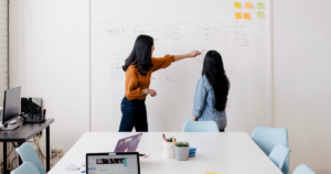 Two people look at sales asset management notes on a large board