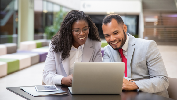 Two people in suits smiling at a computer