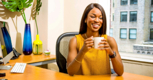 Person holds cup and smiles while sitting at a desk