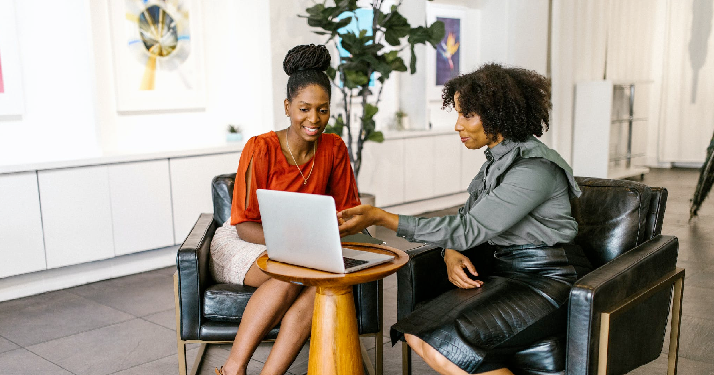 Two people in chairs look at a laptop while discussing sales enablement